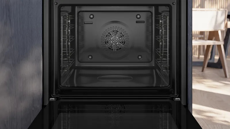 Vista interna di un forno da incasso nero vuoto con griglie laterali e ventola posteriore.