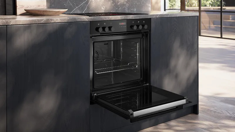 Moderno forno nero da incasso con porta aperta in una cucina buia.