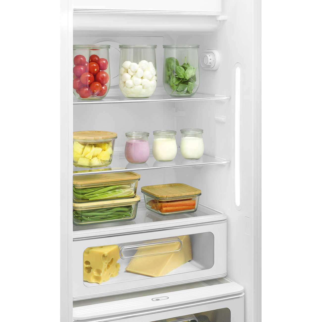 Un frigorifero bianco pieno di barattoli di verdure, frutta, latticini e formaggio sui ripiani.