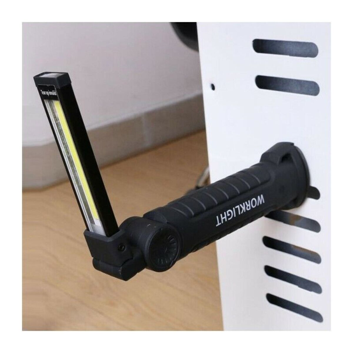Eine schwarze Arbeitsleuchte mit leuchtendem COB-LED-Streifen ist magnetisch an einer weißen Metalloberfläche befestigt.