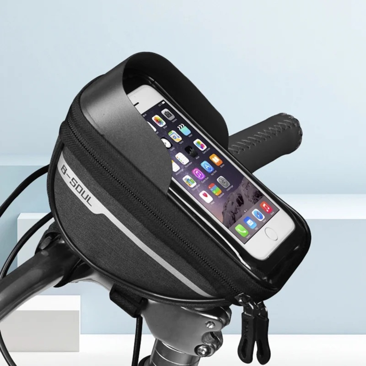 Eine schwarze Fahrrad-Lenkertasche mit einem Smartphone oben drauf, vor hellen Hintergrund.