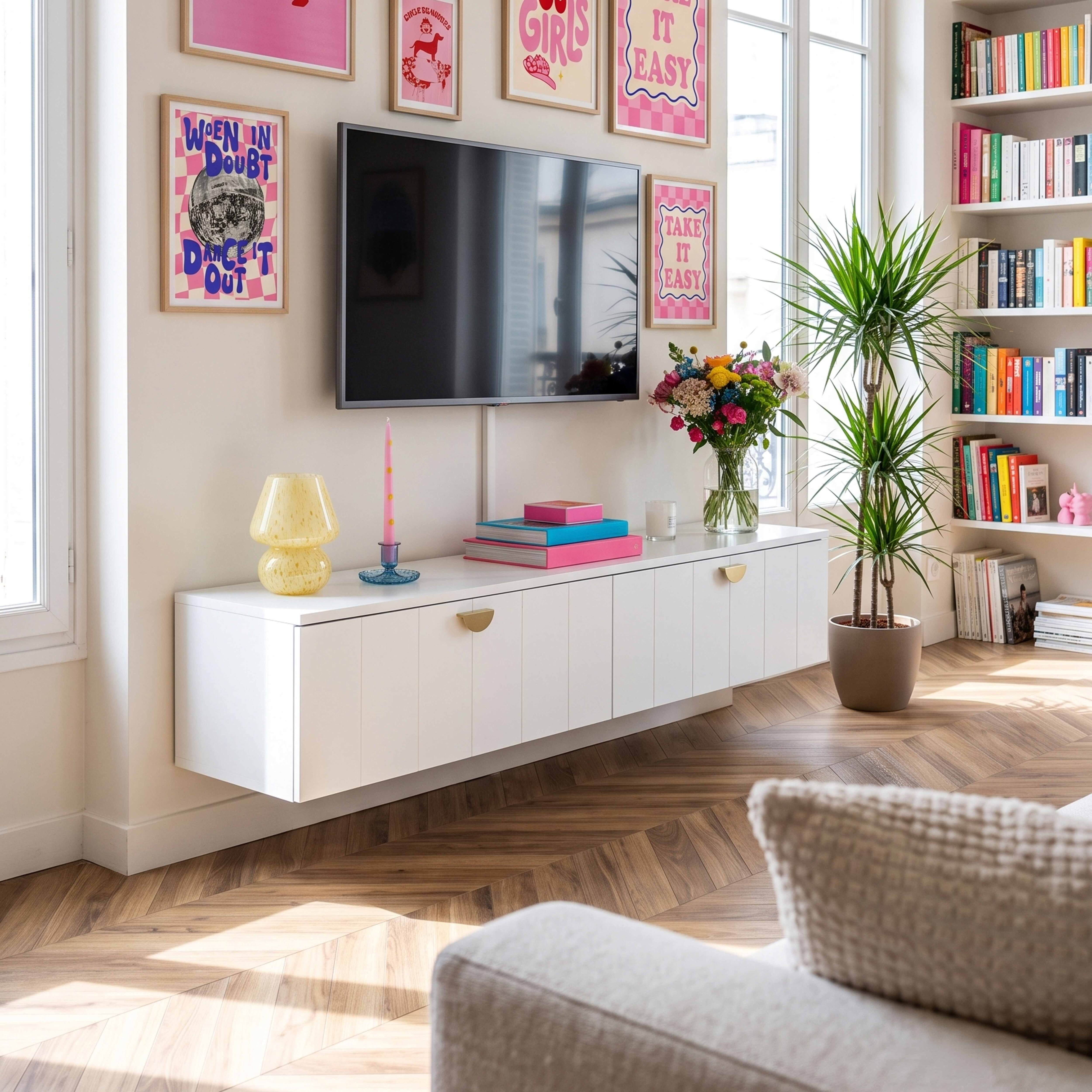 Wohnzimmer mit weißem Schrank, Fernseher, bunten Postern, Pflanzen und Regalen mit Büchern.