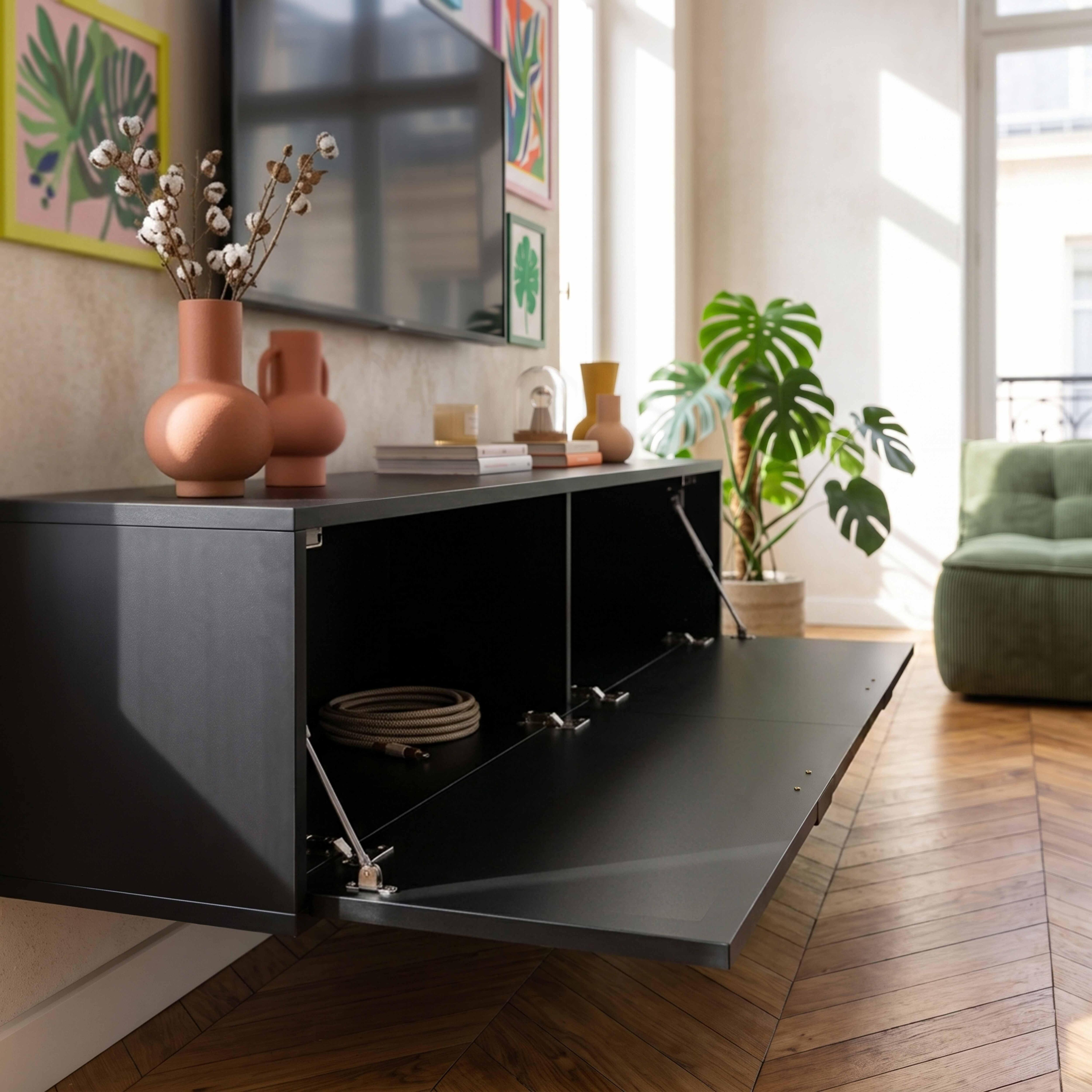 Ein schwarzer, schwebender Schrank mit geöffneter Klappe, dekoriert mit Vasen und Pflanzen im Hintergrund.