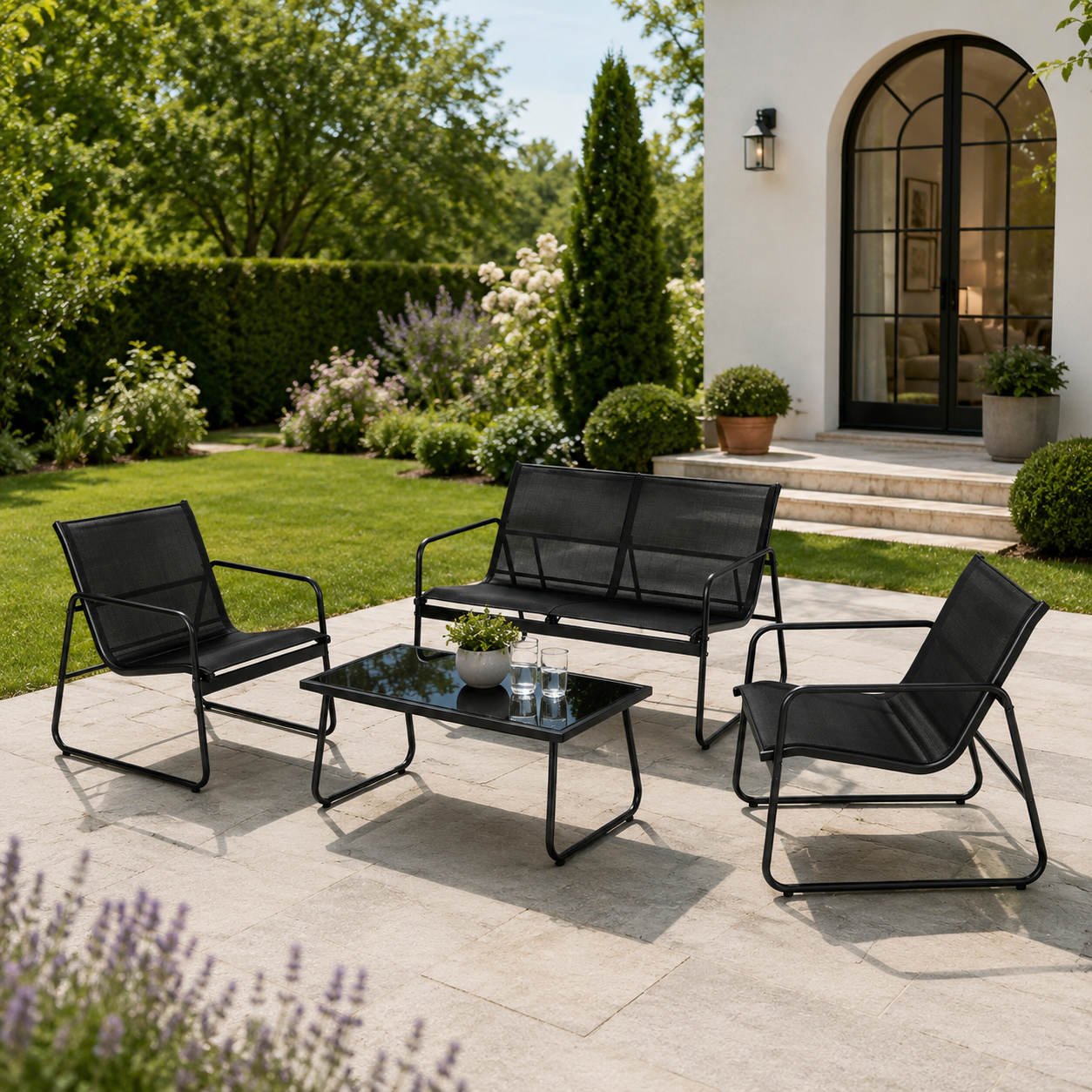 Muebles de jardín negros con un sofá, dos sillones y una mesa en una terraza de piedra ante una casa blanca.