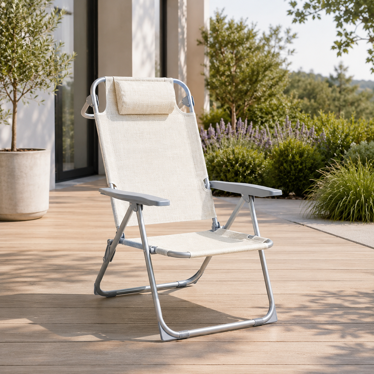 Una silla plegable beige en una terraza de madera frente a una casa con jardín al fondo.