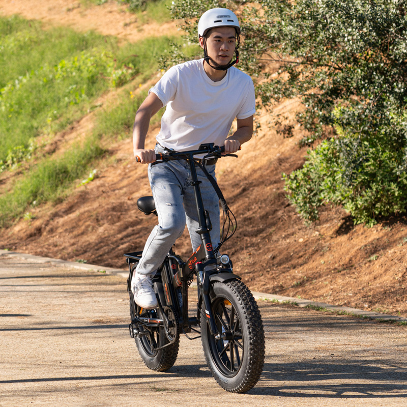 Un joven con casco y camiseta blanca monta en una bicicleta eléctrica negra por un camino.
