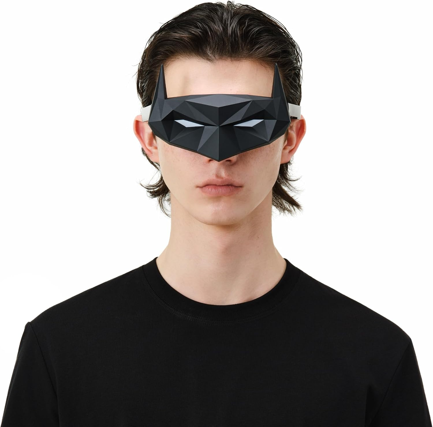 Siyah tişörtlü bir adam, beyaz arka plan önünde siyah geometrik bir Batman maskesi takıyor.