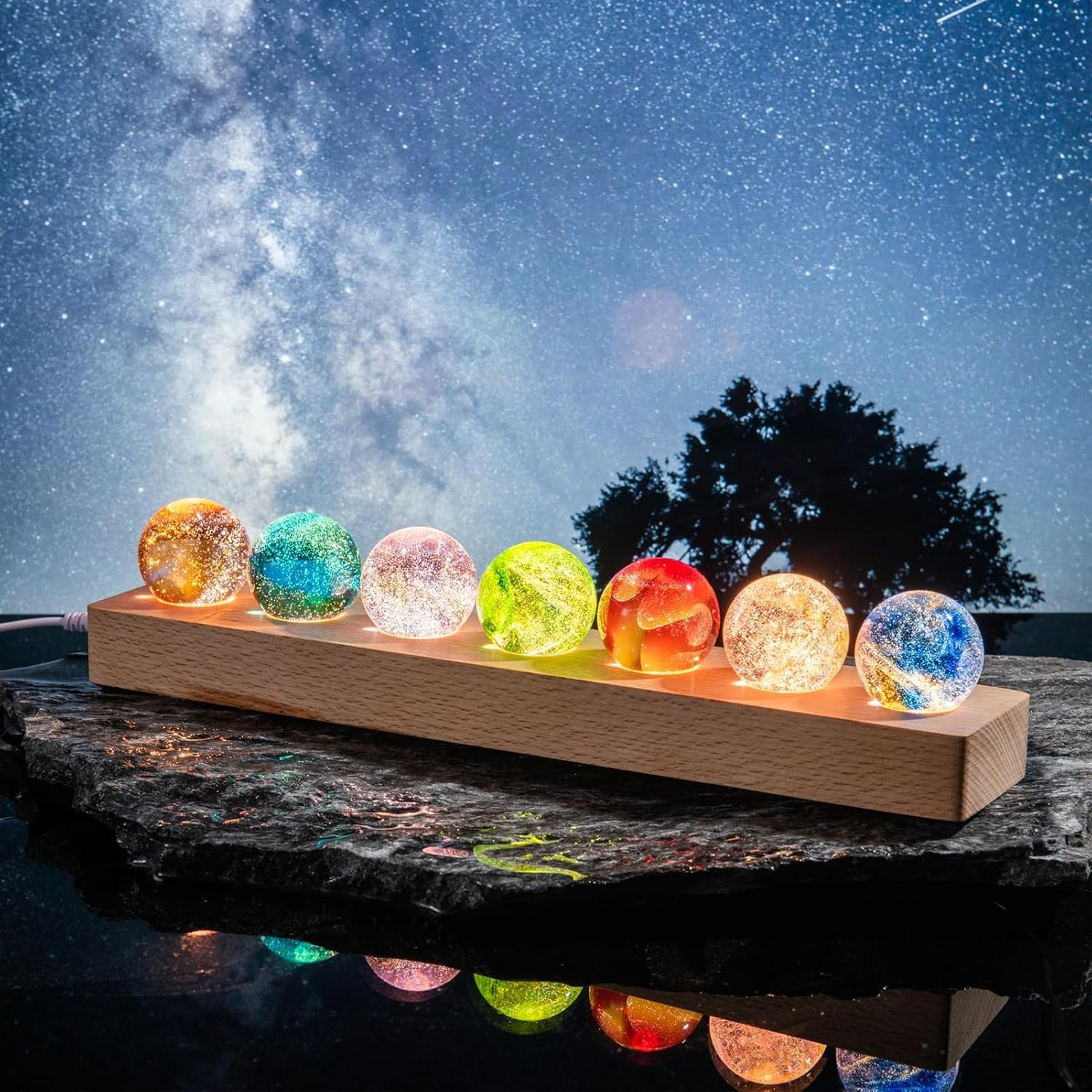 Sieben beleuchtete, glitzernde Kugeln auf einem Holzsockel vor einem sternenklaren Nachthimmel.