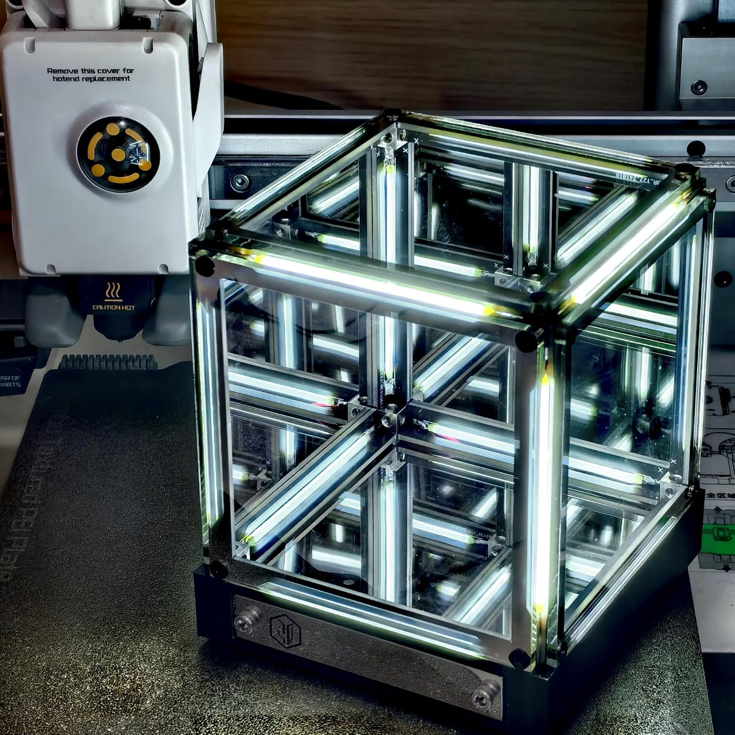 Ein beleuchteter Spiegelwürfel steht vor einer 3D-Druckerdüse.