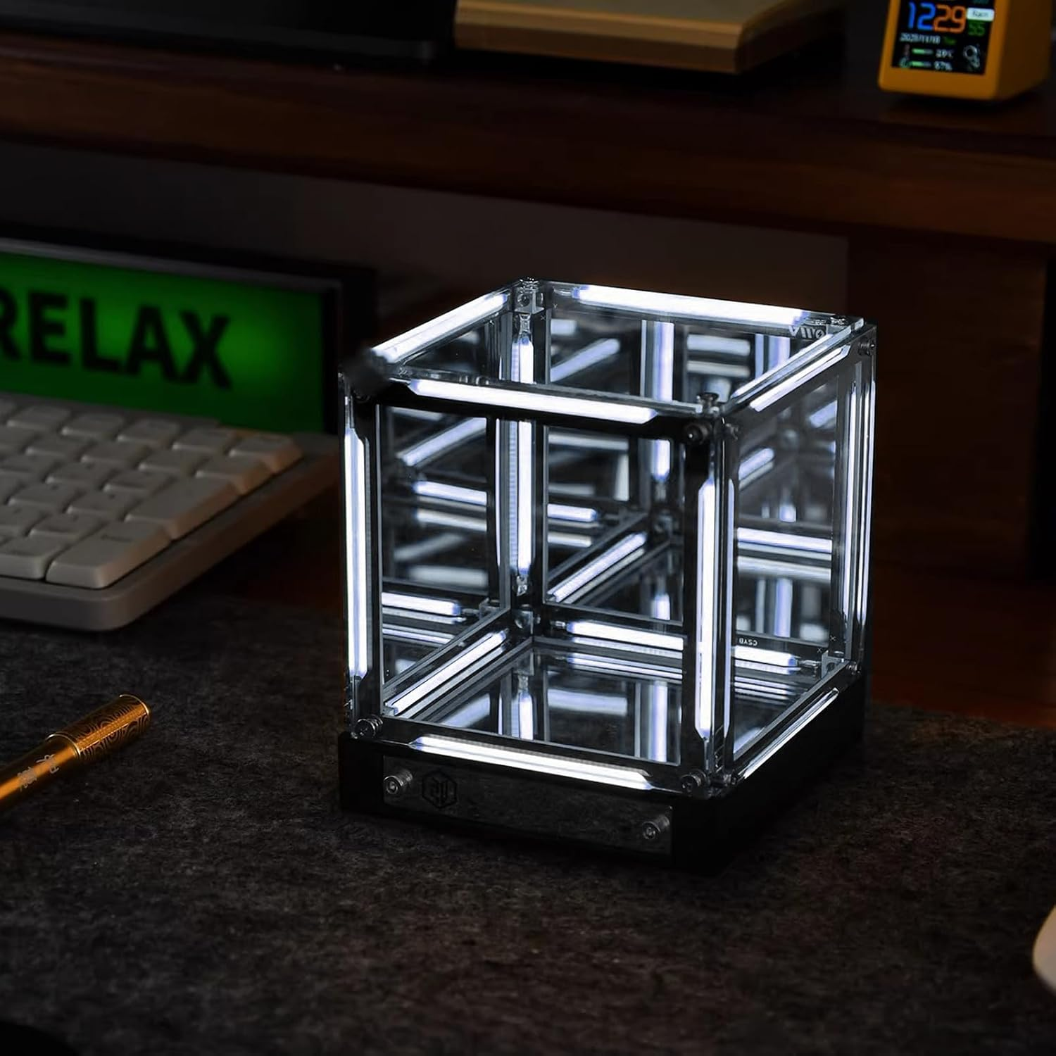 Ein beleuchteter, spiegelnder LED-Würfel auf einem dunklen Schreibtisch neben einer Tastatur.