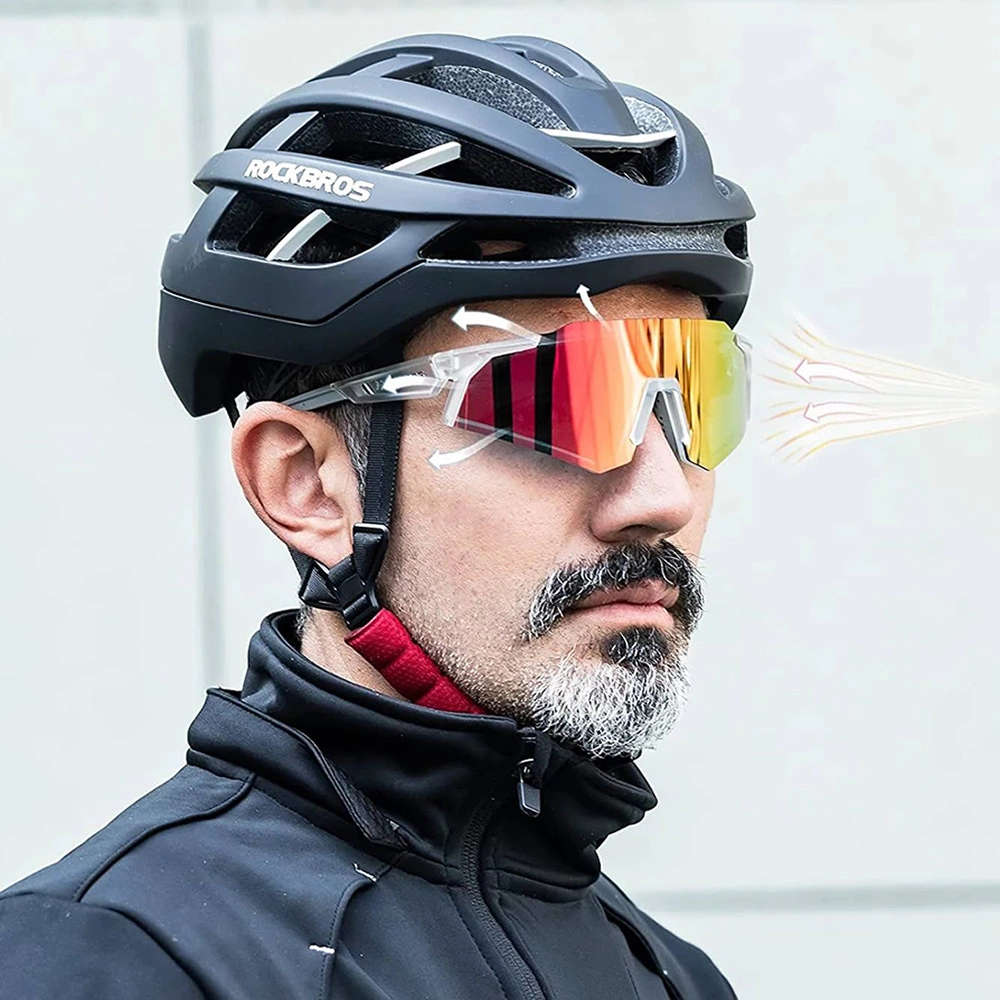 Un uomo con casco da bici nero e occhiali da sole sportivi su sfondo grigio.