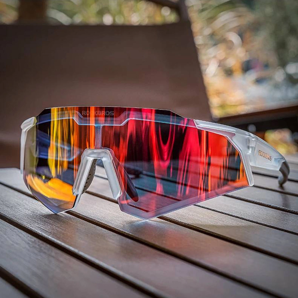 Moderni occhiali da sole sportivi con montatura bianca e lenti specchiate rosso-giallo su tavolo di legno.