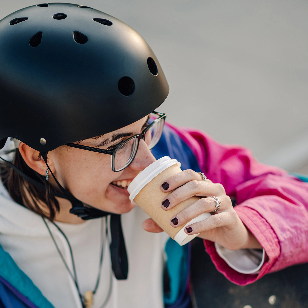 Una persona con casco nero e occhiali beve caffè da un bicchiere di carta.