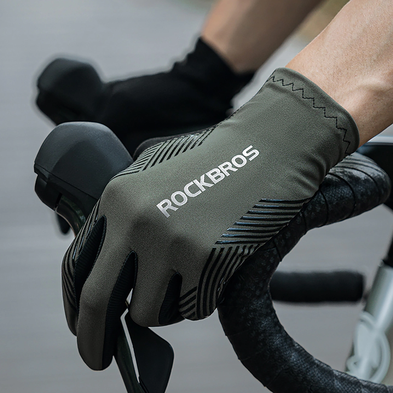 La mano di un ciclista con un guanto verde oliva Rockbros afferra il manubrio e la leva del freno.