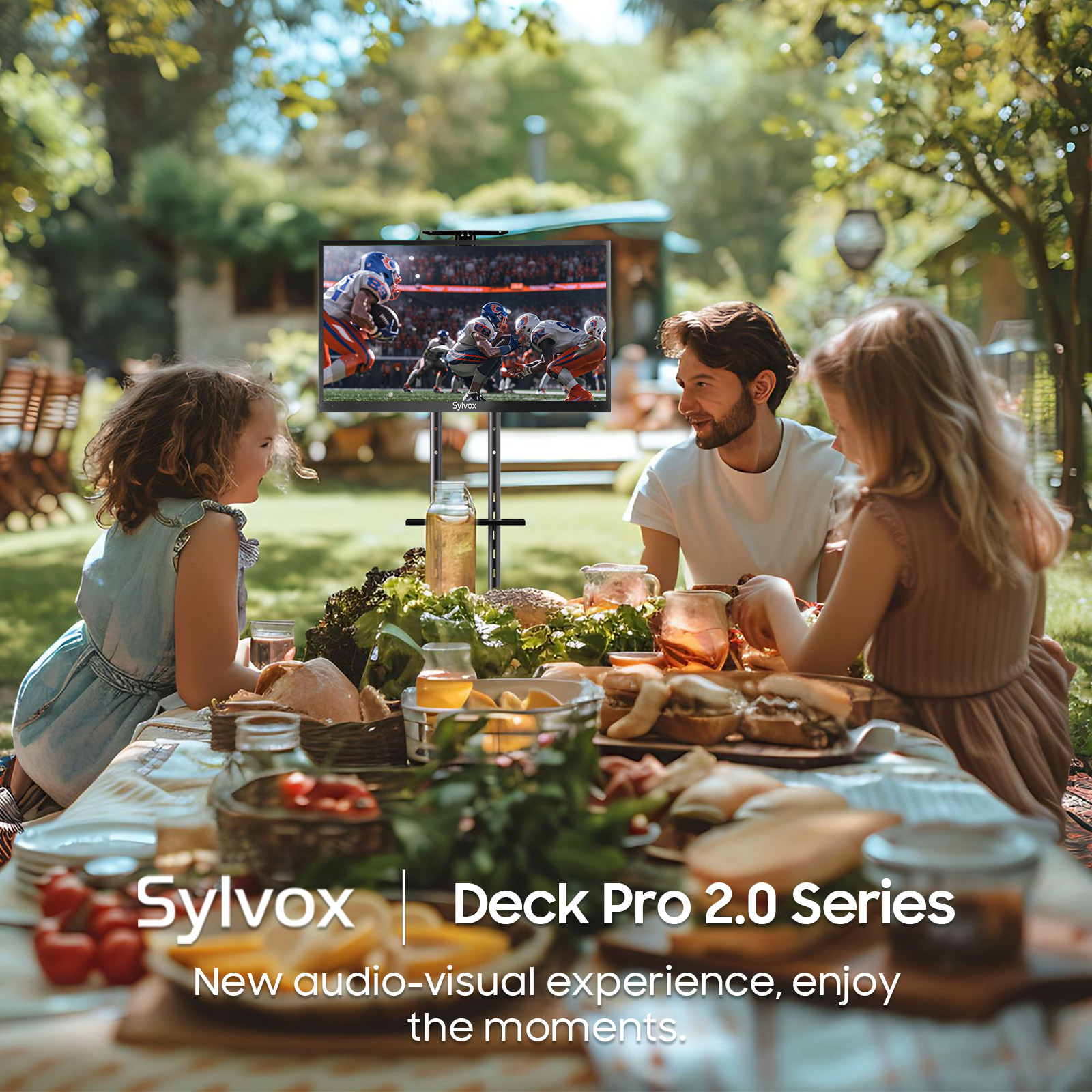 Eine Familie genießt ein Picknick im Garten, während ein Fernseher ein Football-Spiel zeigt.