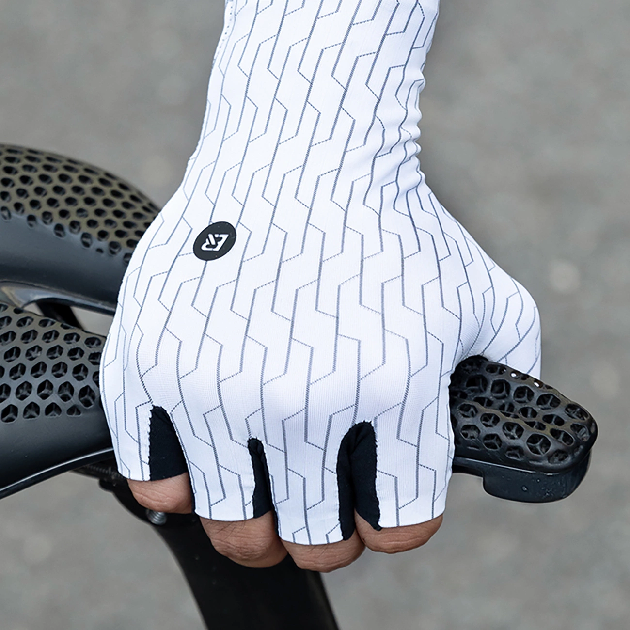 Mano con guanto da ciclismo bianco a motivi geometrici afferra il manubrio con motivo a nido d'ape di una bicicletta.