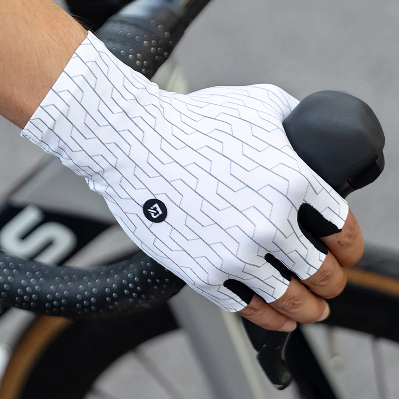 Una mano che indossa un guanto da ciclismo con motivo bianco e grigio afferra il manubrio di una bicicletta.