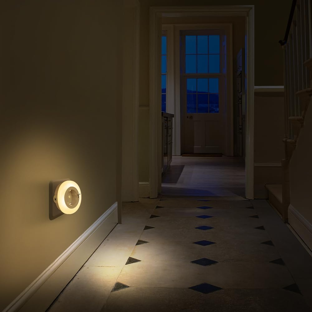 Ein kleines warmes Nachtlicht leuchtet in einem dunklen Flur mit Steinboden und einer Treppe.