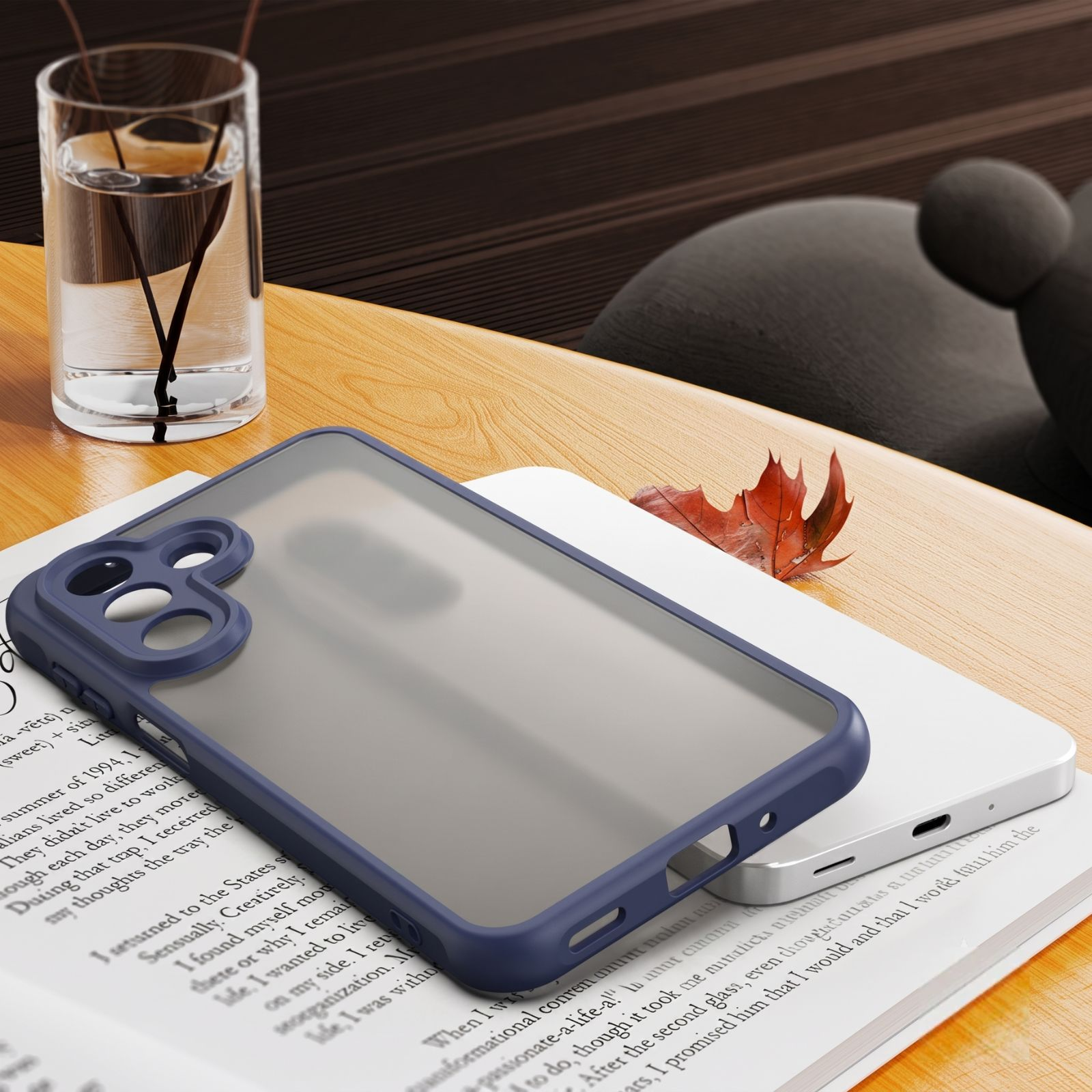 Blaue Smartphone-Hülle und ein weißes Telefon auf einem offenen Buch, mit einem Glas Wasser und einem herbstlichen Blatt auf einem Holztisch.