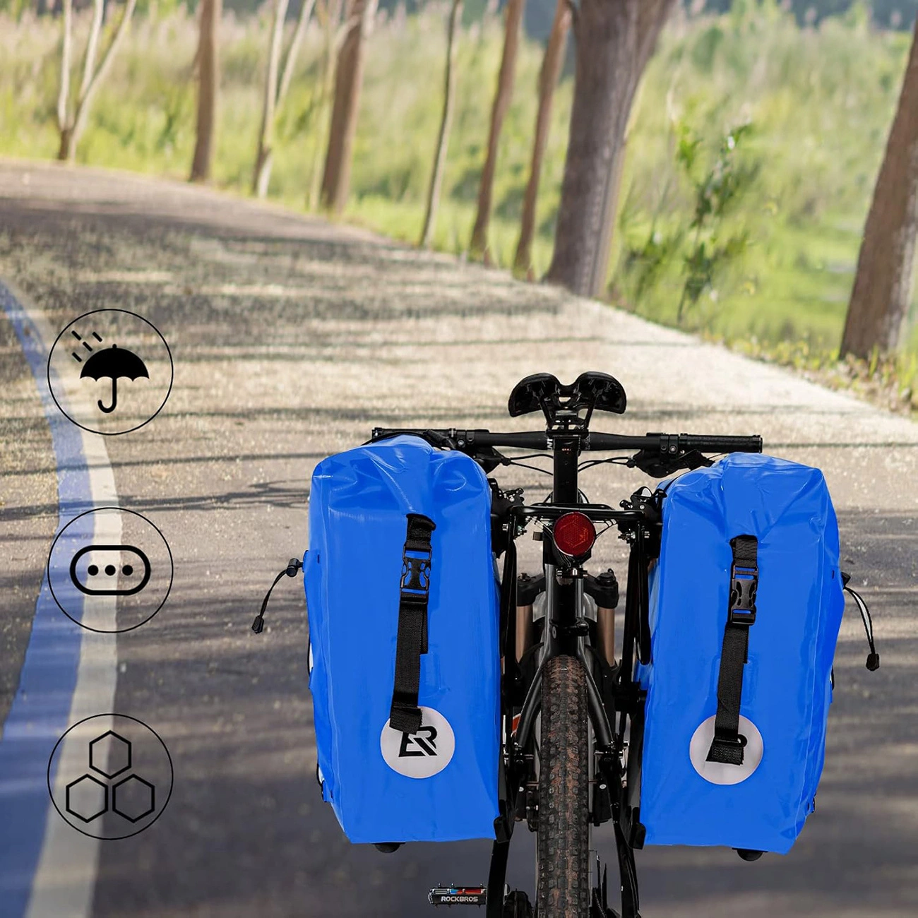 Una bicicletta con due borse laterali impermeabili blu vivo su un sentiero alberato.