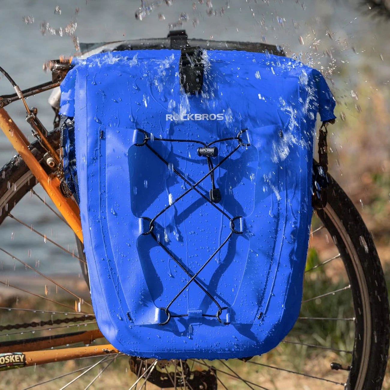 Borsa da bicicletta blu Rockbros attaccata a una bici arancione con schizzi d'acqua.