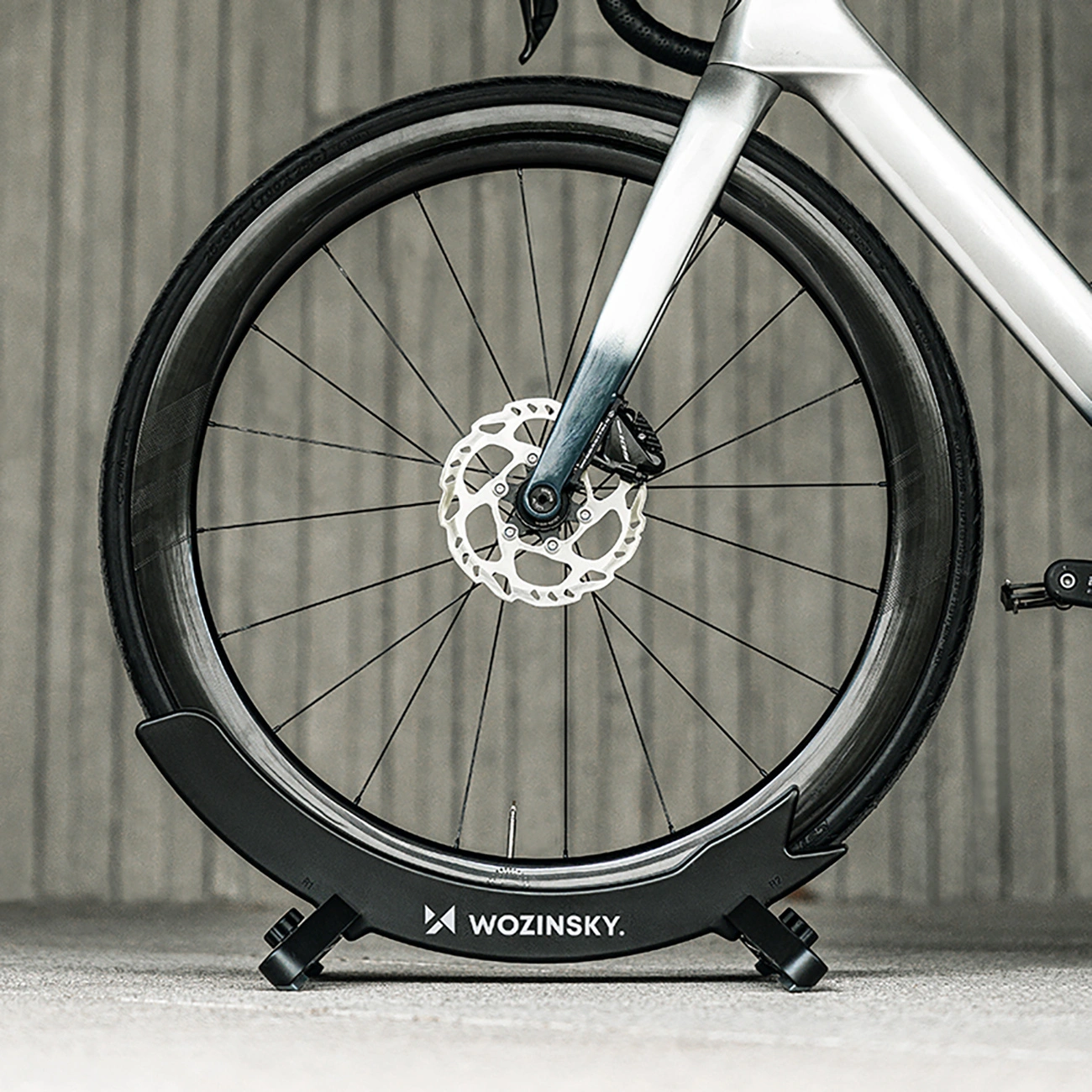 Una ruota anteriore di bicicletta fissata in un supporto nero Wozinsky contro una parete.