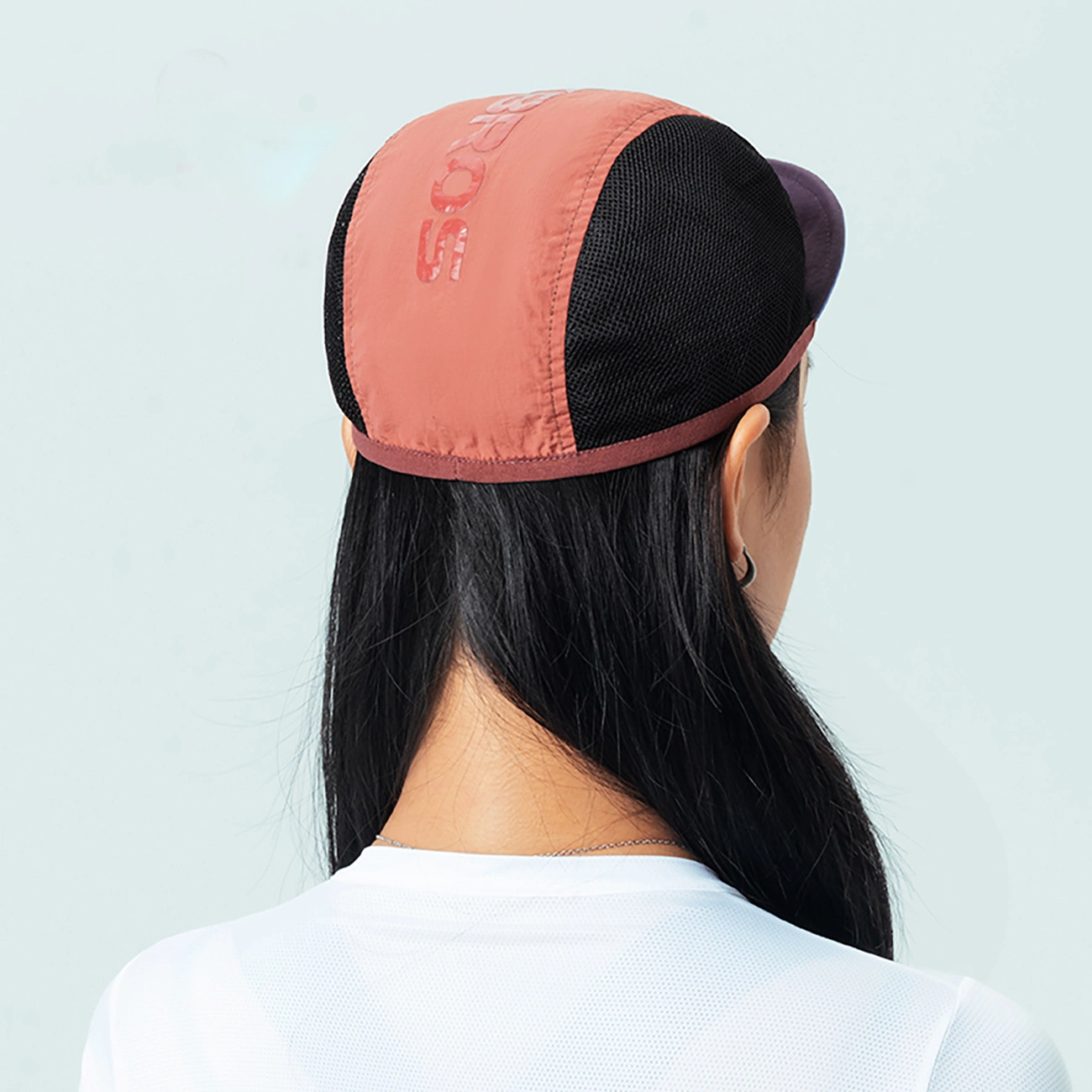Vista posteriore di una persona con capelli neri che indossa un berretto rosa e nero e una maglietta bianca.