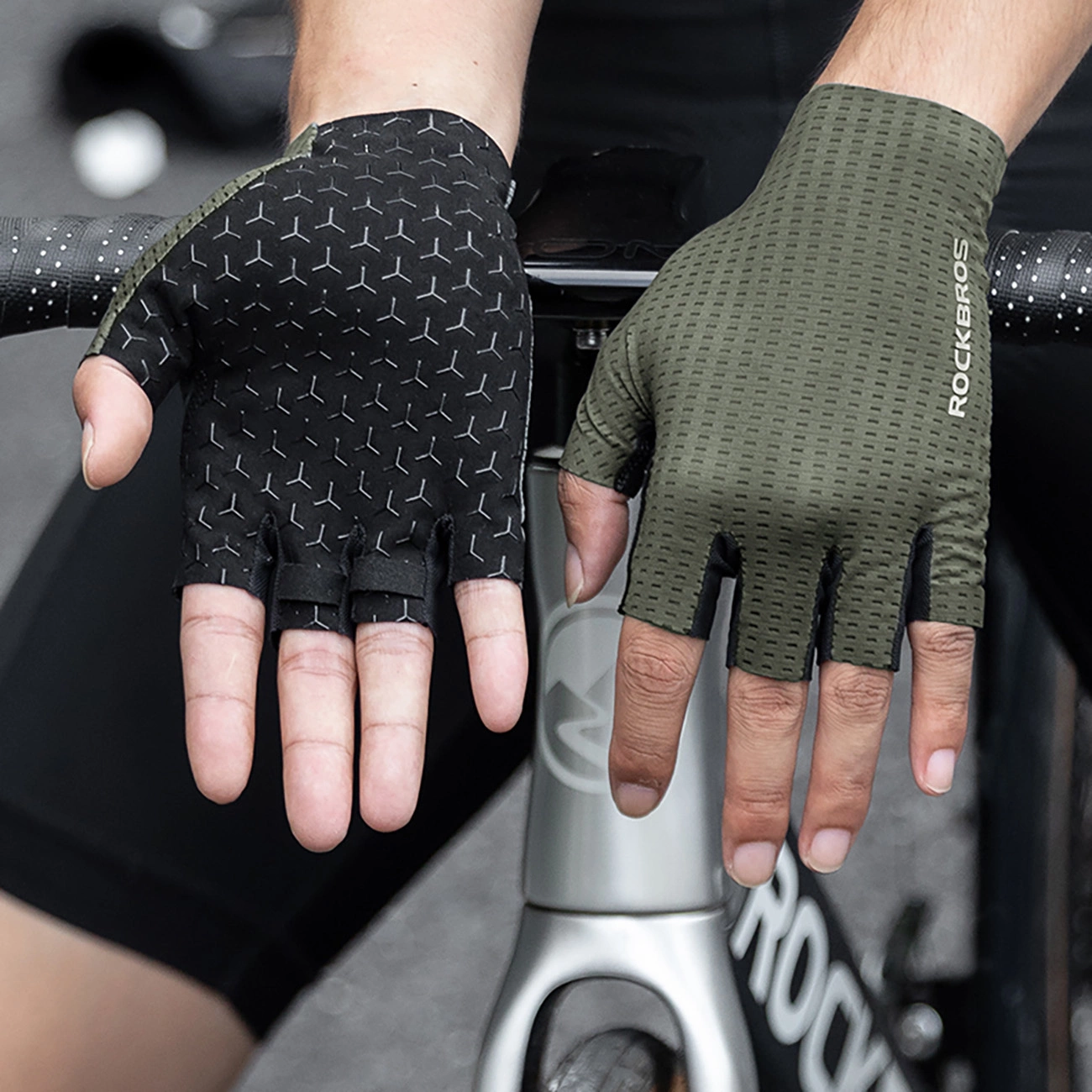 Un ciclista mostra un guanto da ciclismo Rockbros nero e uno verde su una bicicletta.