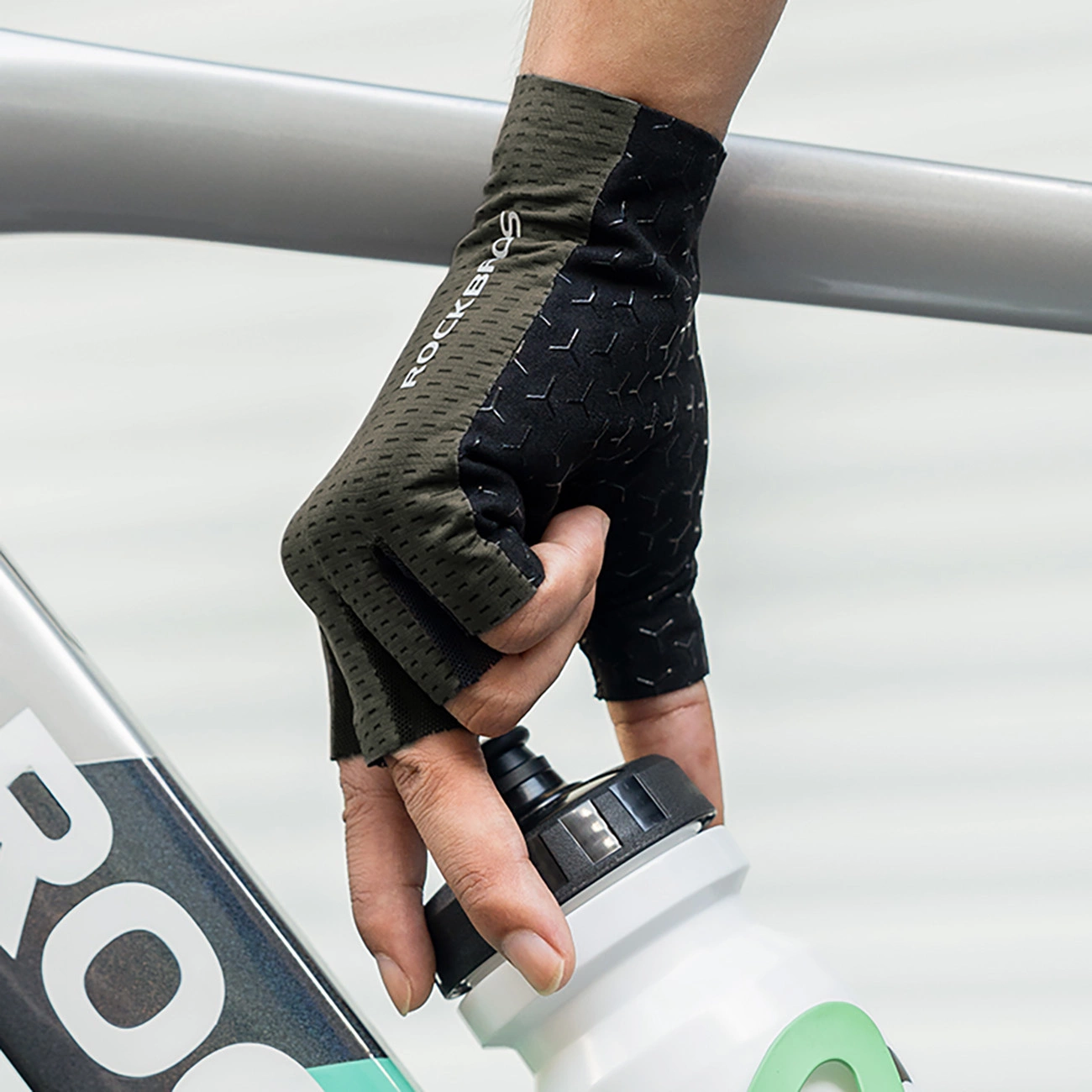 Una mano con guanto da ciclismo tiene una borraccia davanti al telaio di una bici.