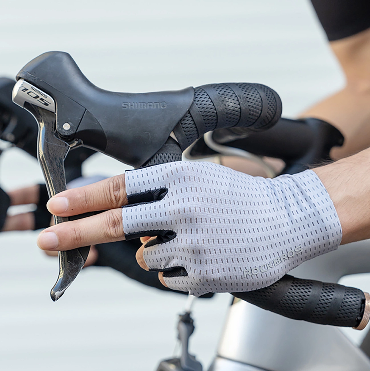 Un ciclista con guanti grigi senza dita afferra il manubrio della bici con una leva Shimano.