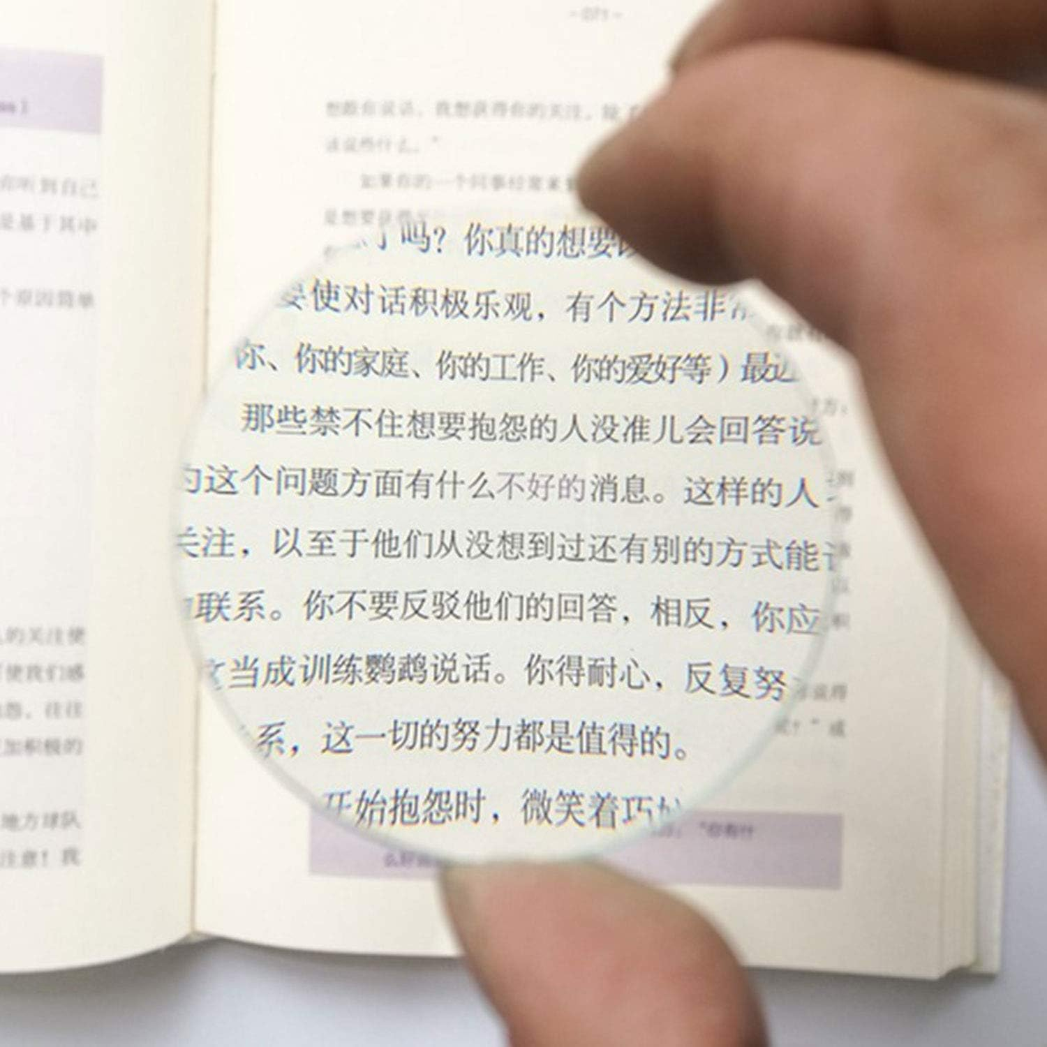 Eine Hand hält eine Lupe über ein offenes Buch mit chinesischem Text.