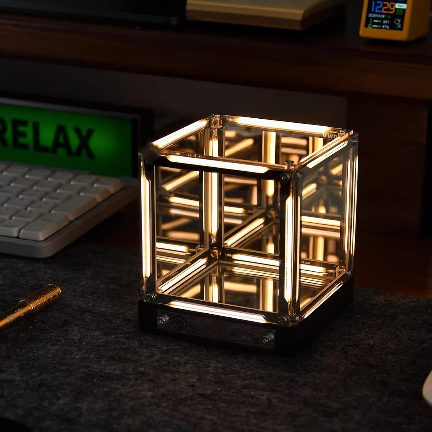 Eine beleuchtete Glaskubuslampe auf einem Schreibtisch mit Tastatur und Uhr.