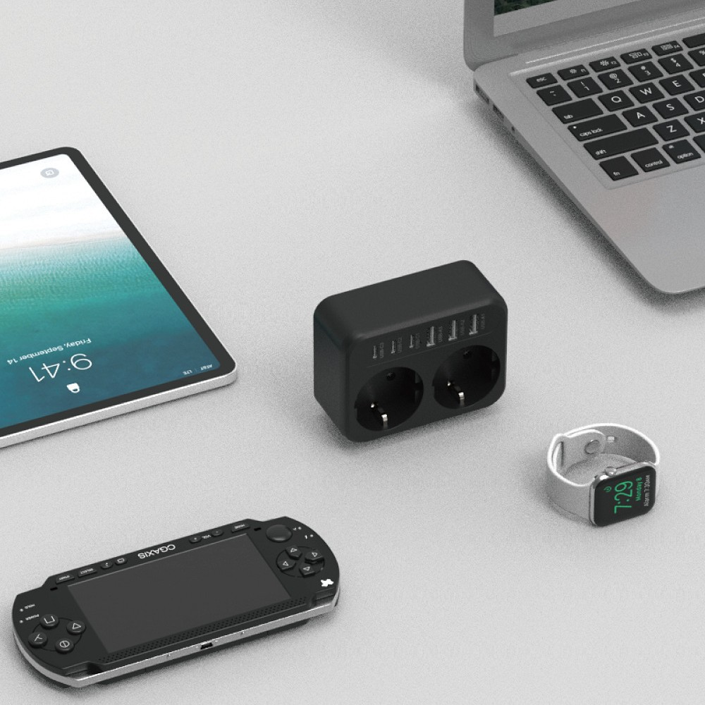 Ein Laptop, Tablet, eine Spielekonsole, eine Smartwatch und eine schwarze Steckdosenleiste mit USB-Anschlüssen auf dem Tisch.