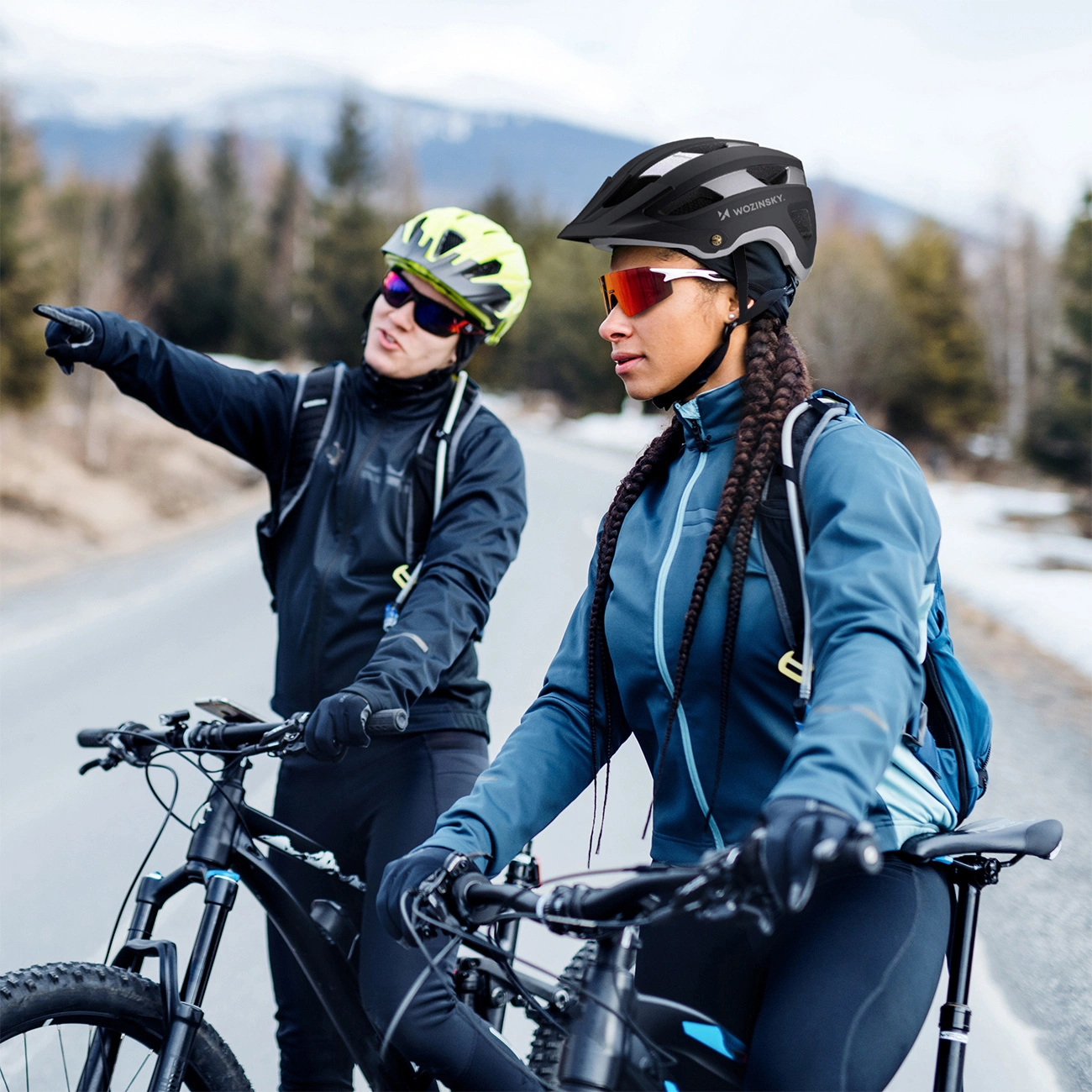 Due ciclisti con caschi e abbigliamento sportivo con biciclette su strada asfaltata, montagne.