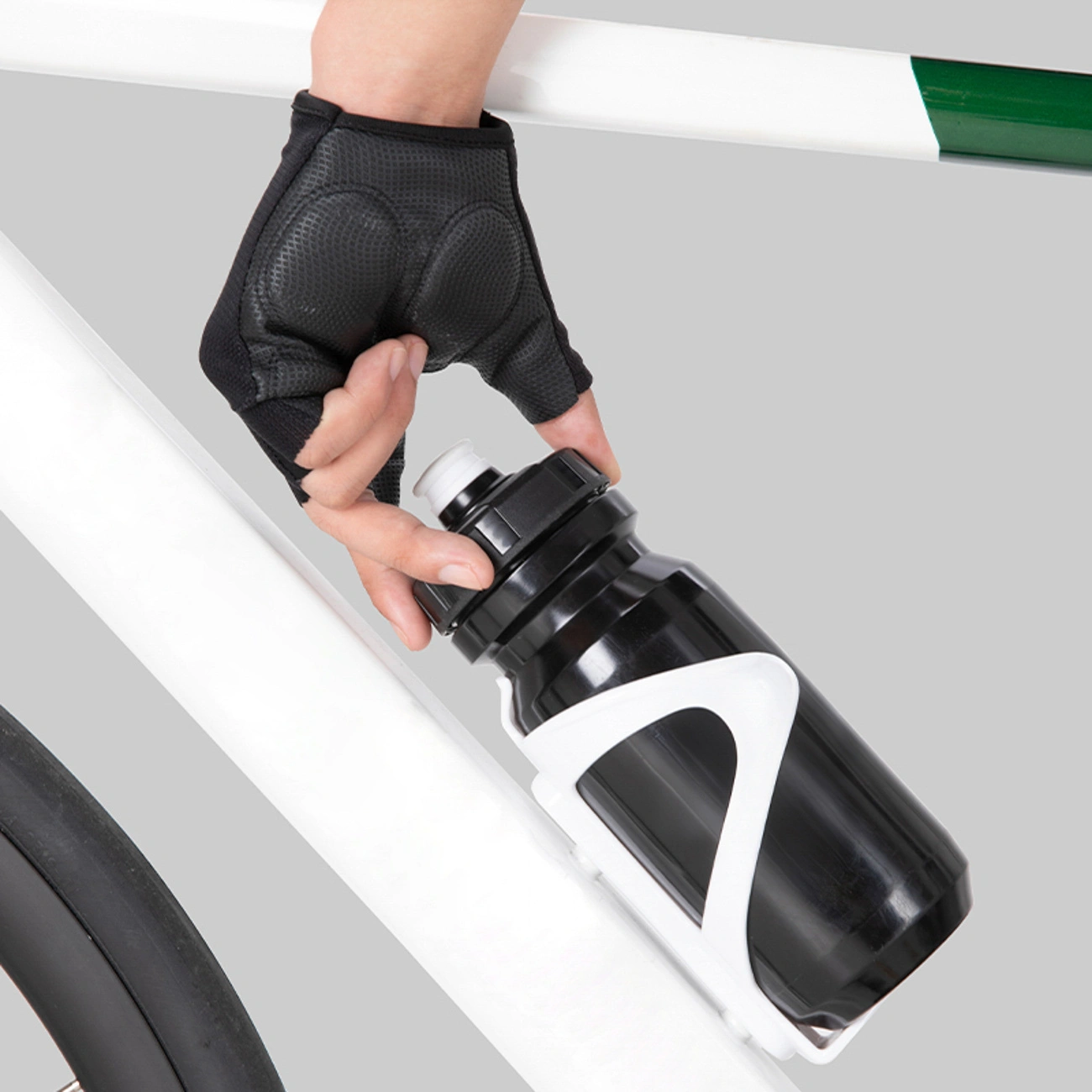 Una mano con un guanto da ciclismo nero estrae una borraccia nera da un portaborraccia bianco su una bicicletta bianca.