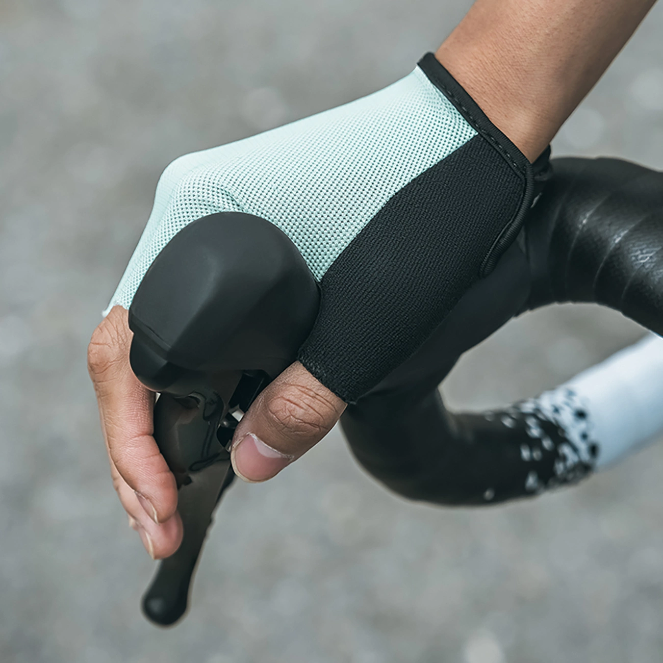 Una mano con un guanto da ciclismo blu e nero afferra la leva del freno di una bici da corsa.
