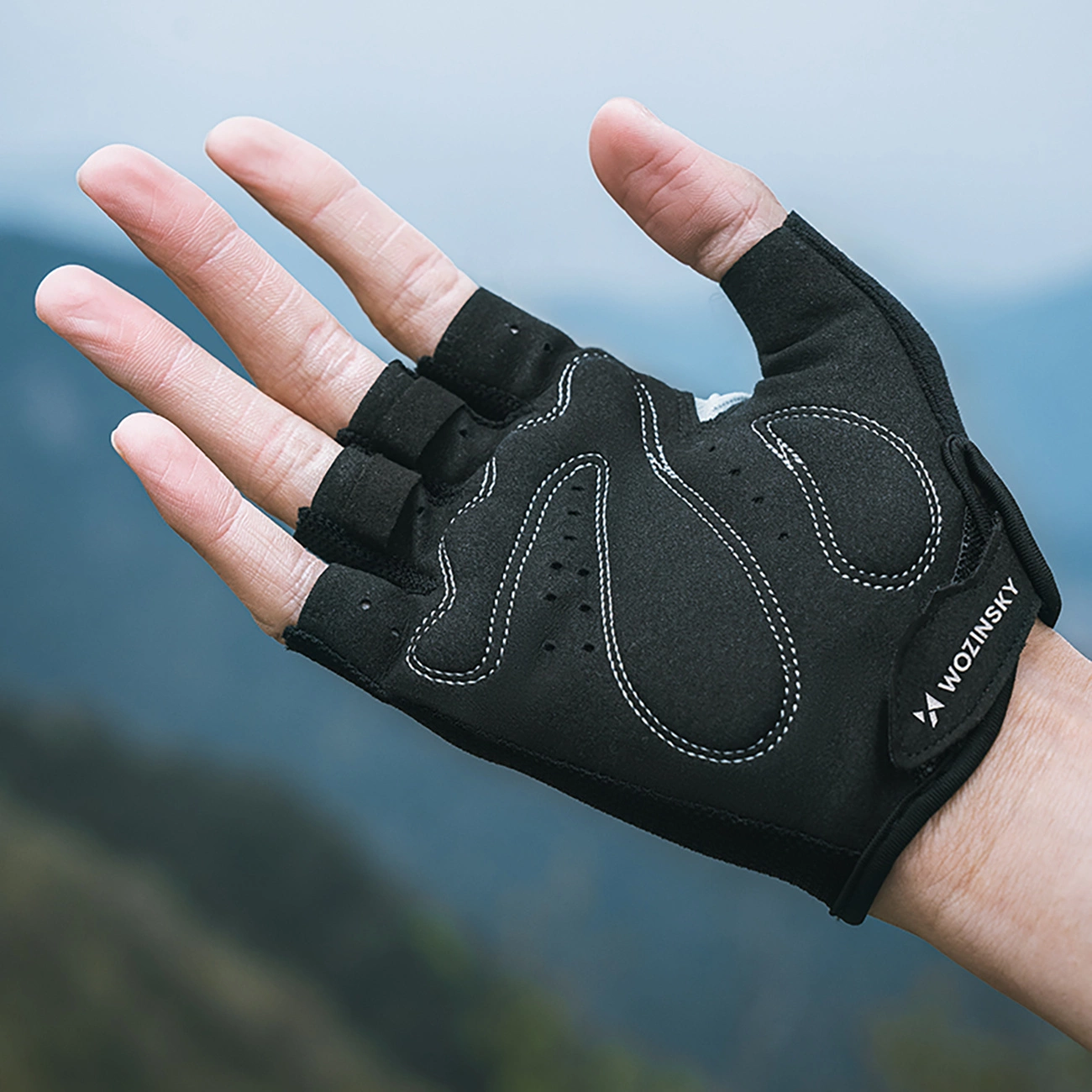 Una mano che indossa un guanto da ciclismo nero senza dita su sfondo sfocato.