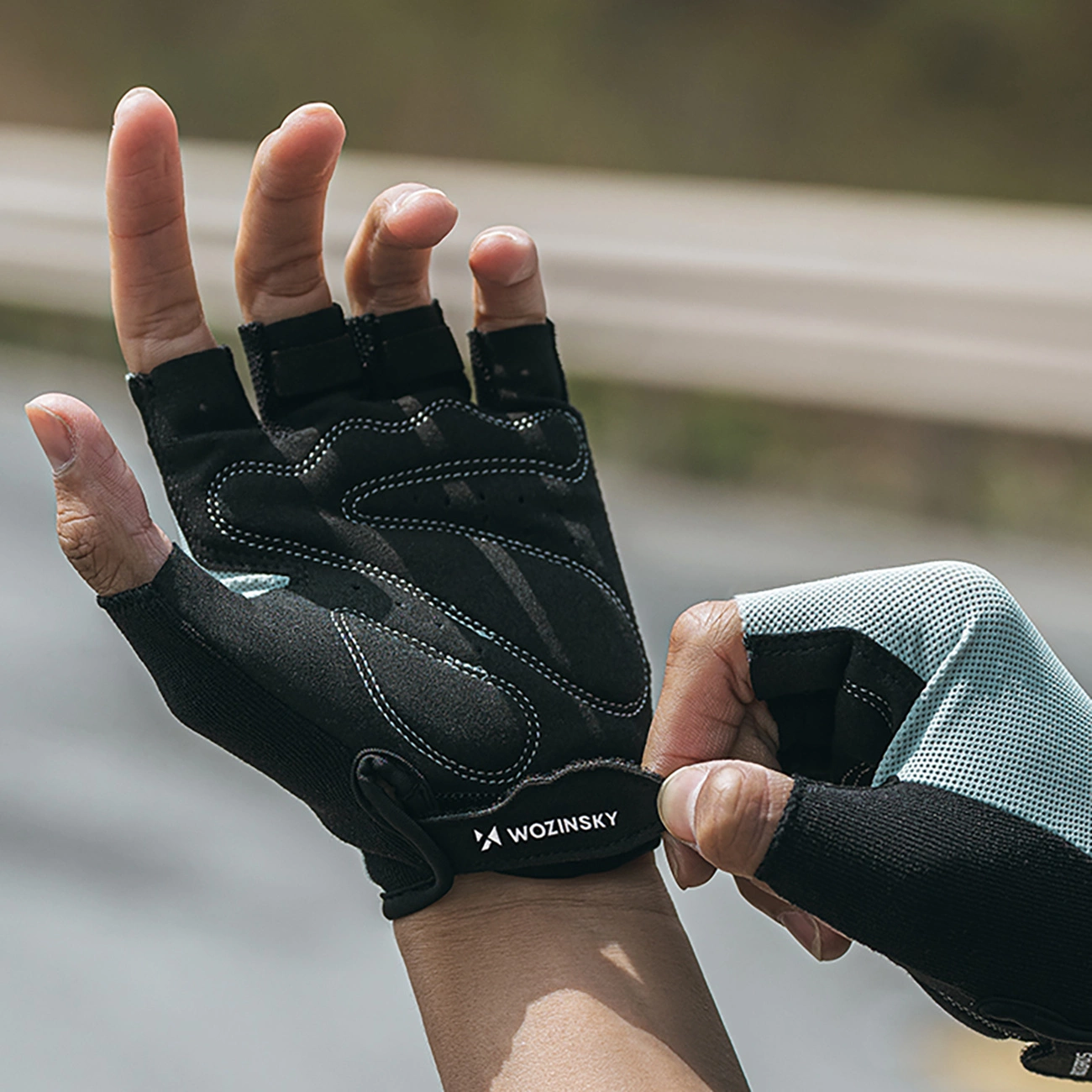 Una persona che indossa guanti da ciclismo neri senza dita con il logo Wozinsky sul polso.