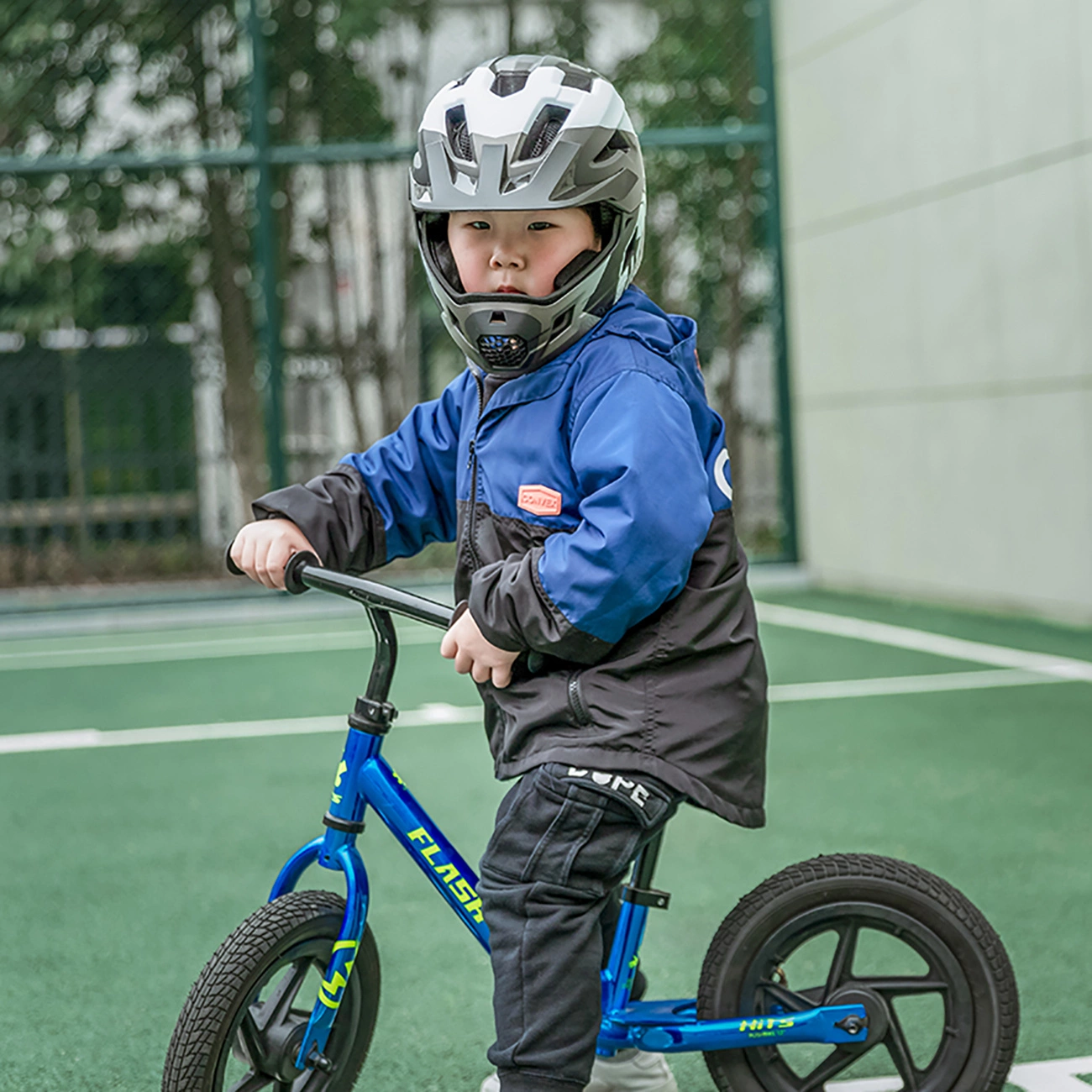 Un bambino con casco e giacca blu guida una bici senza pedali blu.