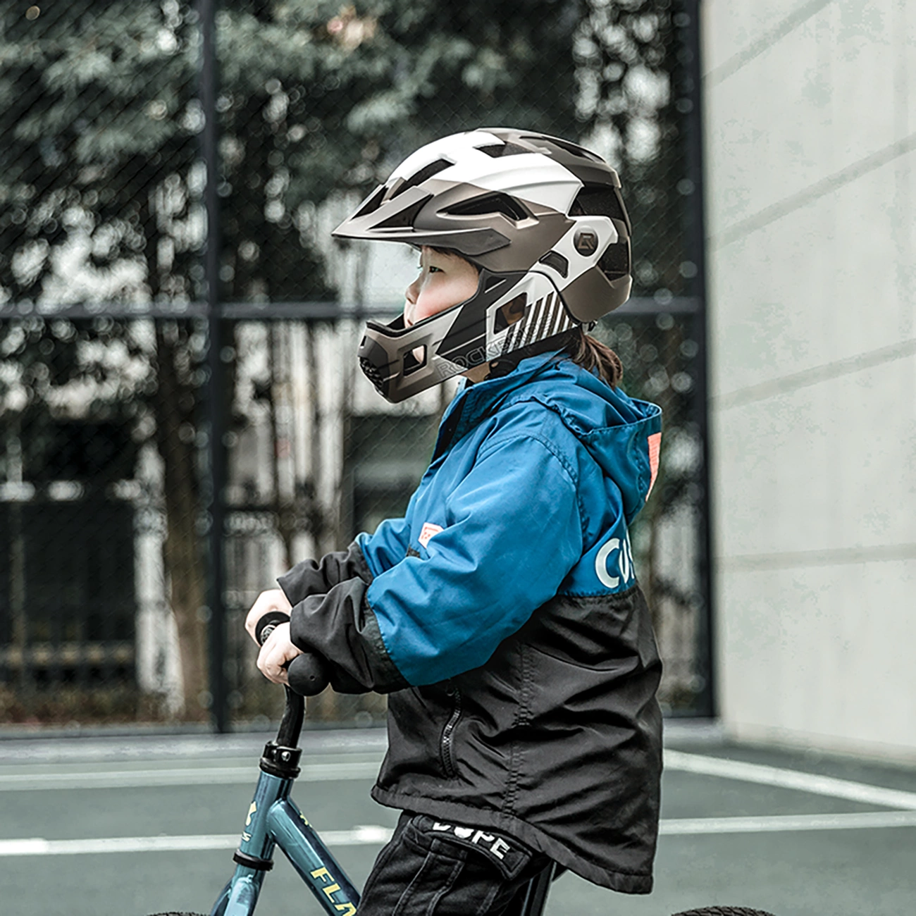 Un bambino con giacca blu e nera e casco va in bicicletta all'aperto.