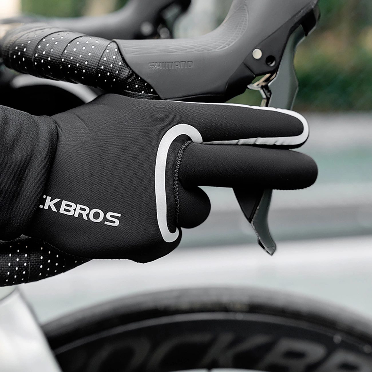 Una mano con un guanto da ciclismo nero Rockbros afferra la leva del freno di una bici da corsa.
