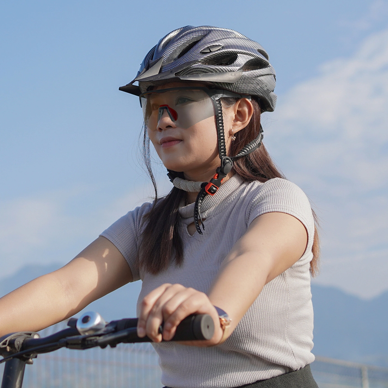 Donna con casco da bici e occhiali che guida una bicicletta sotto un cielo azzurro.
