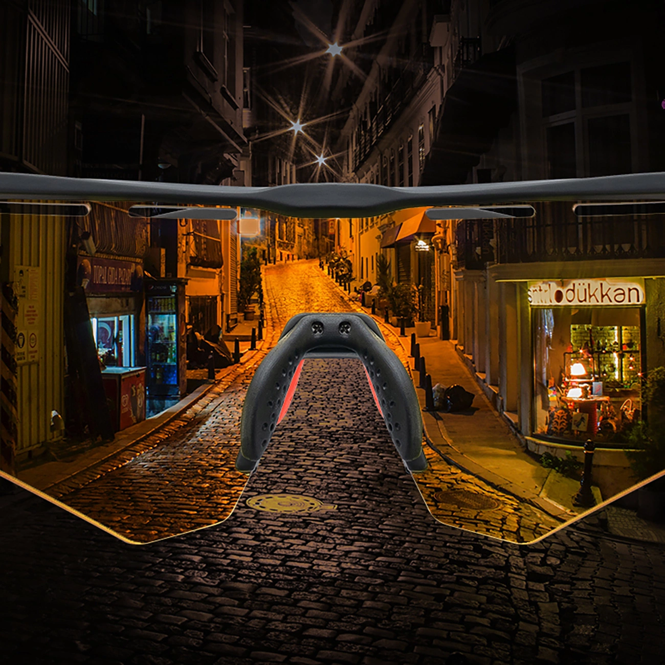 Vista attraverso occhiali sportivi di una strada notturna acciottolata del centro storico con negozi illuminati.