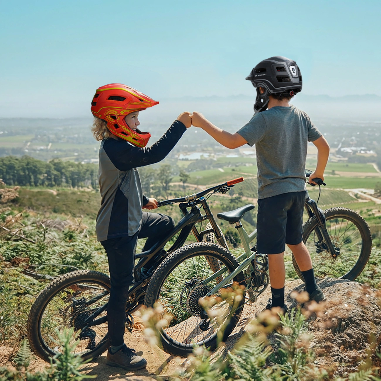 Due giovani ciclisti con casco si danno il pugno su una collina con mountain bike.