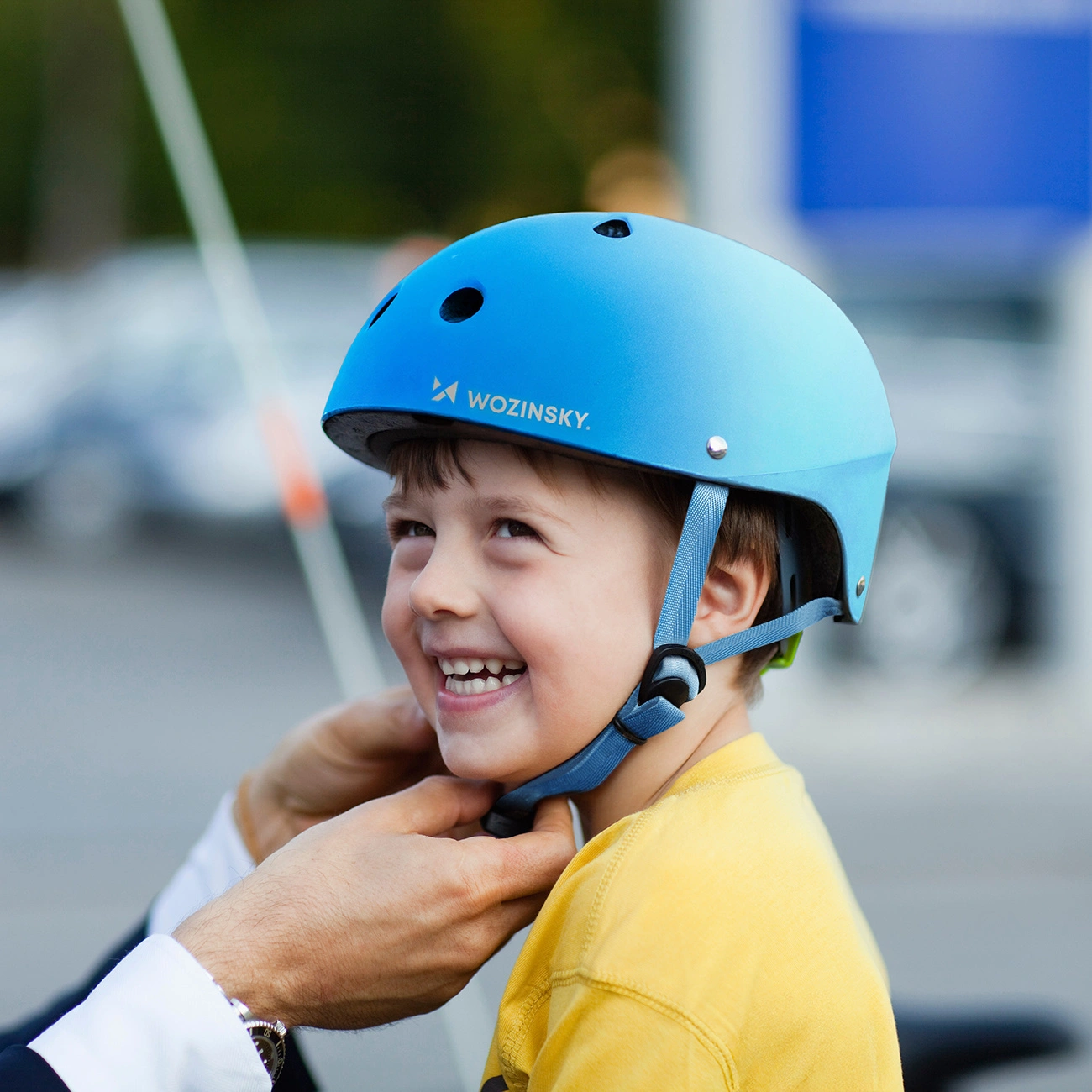 Un bambino felice con una maglietta gialla sorride mentre gli mettono un casco blu Wozinsky.