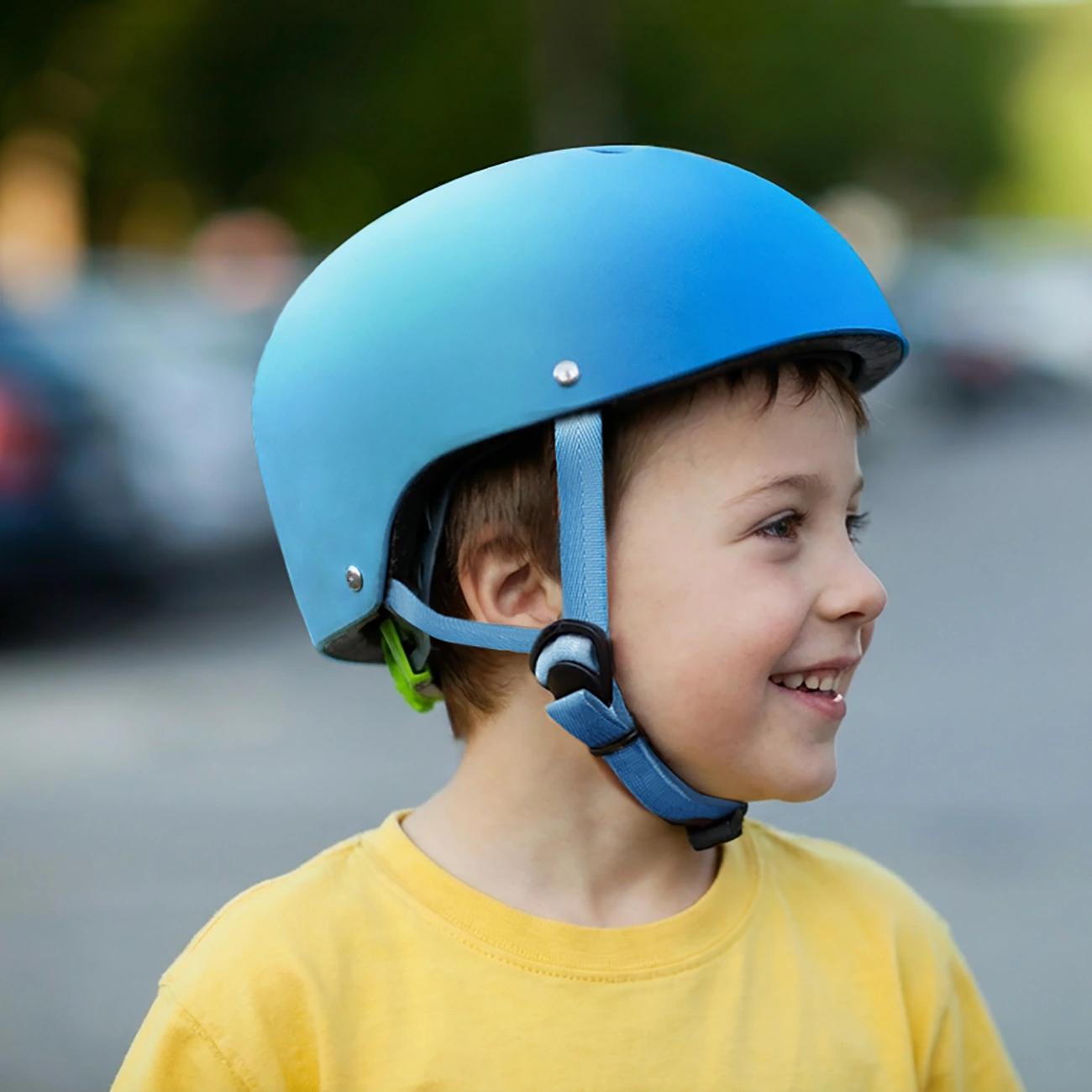Un bambino con maglietta gialla e casco blu sorride davanti a uno sfondo sfocato.