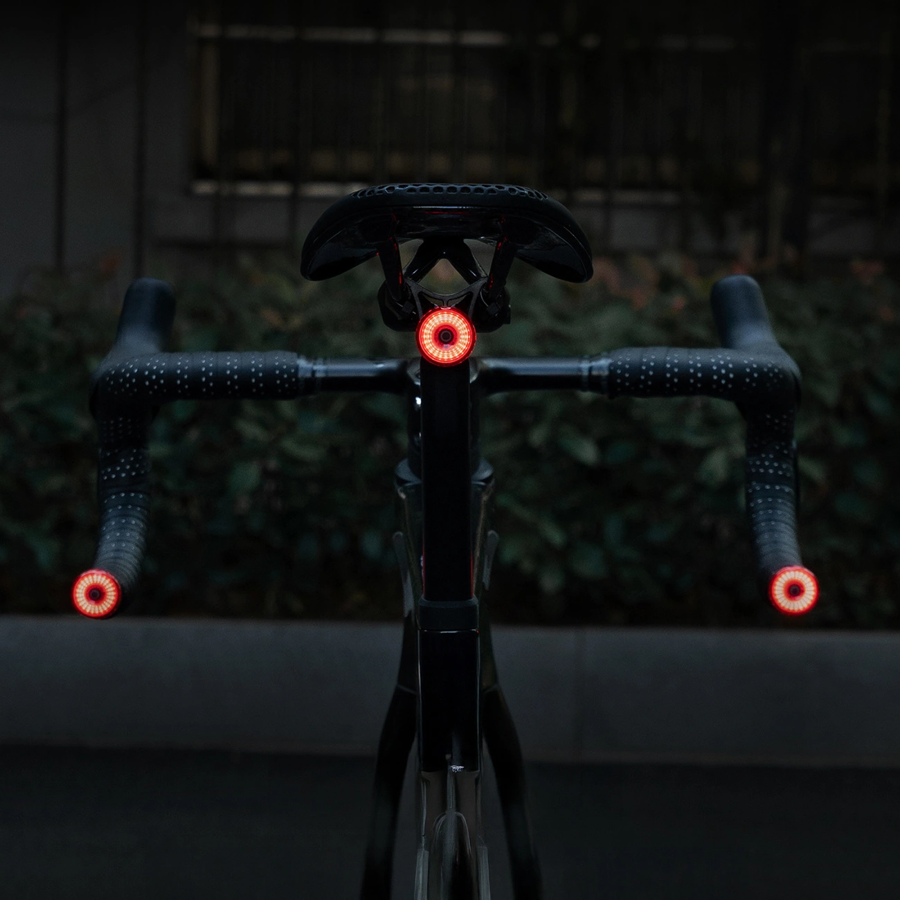 Vista posteriore di una bicicletta di notte, con luci rosse brillanti sul manubrio e sotto la sella.