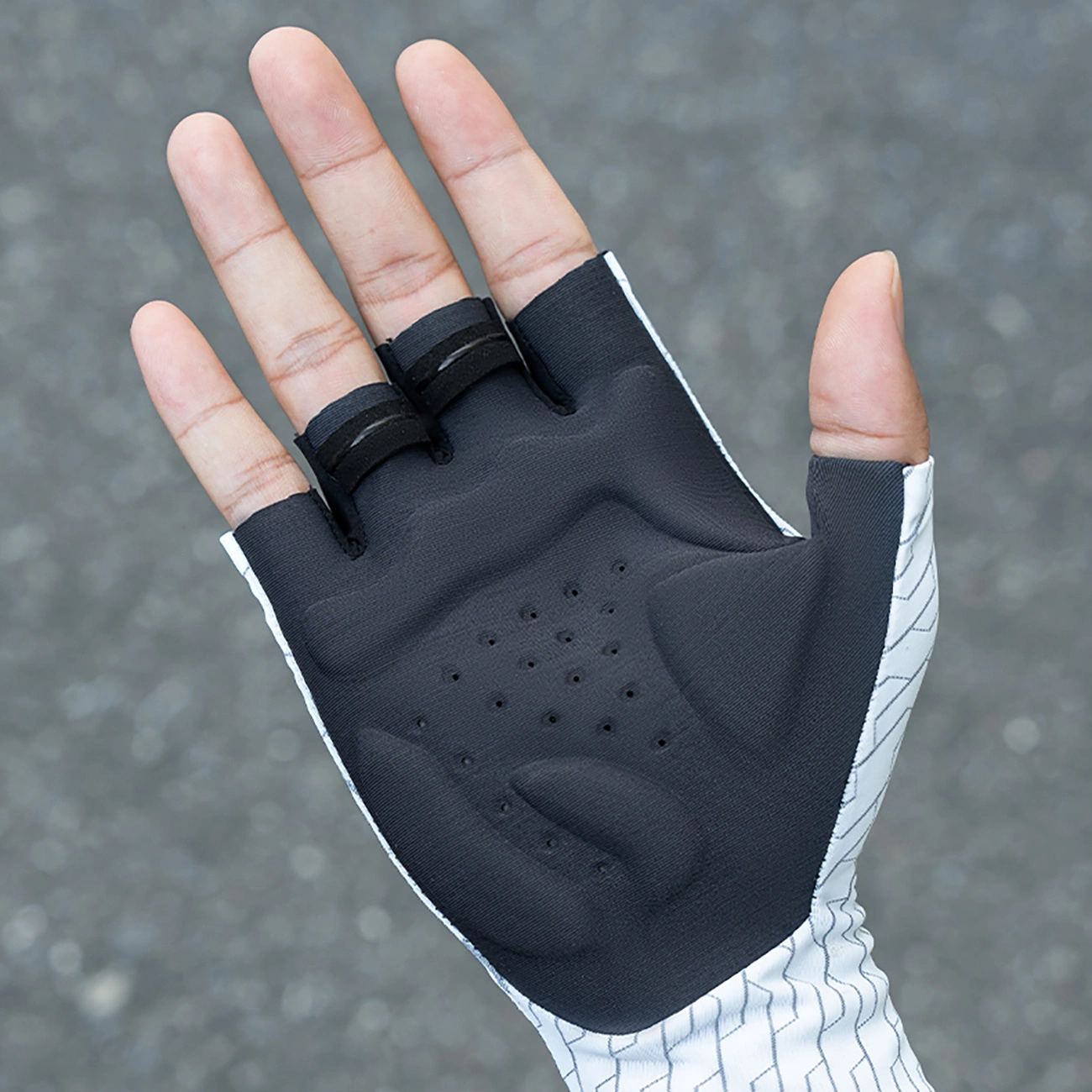 Una mano indossa un guanto da ciclismo senza dita nero e bianco con imbottitura.