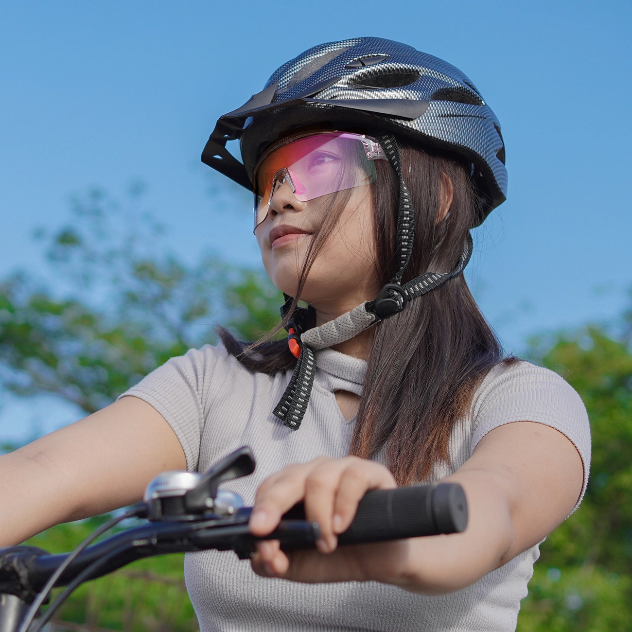 Donna con casco e occhiali rosa va in bicicletta sotto il cielo blu.