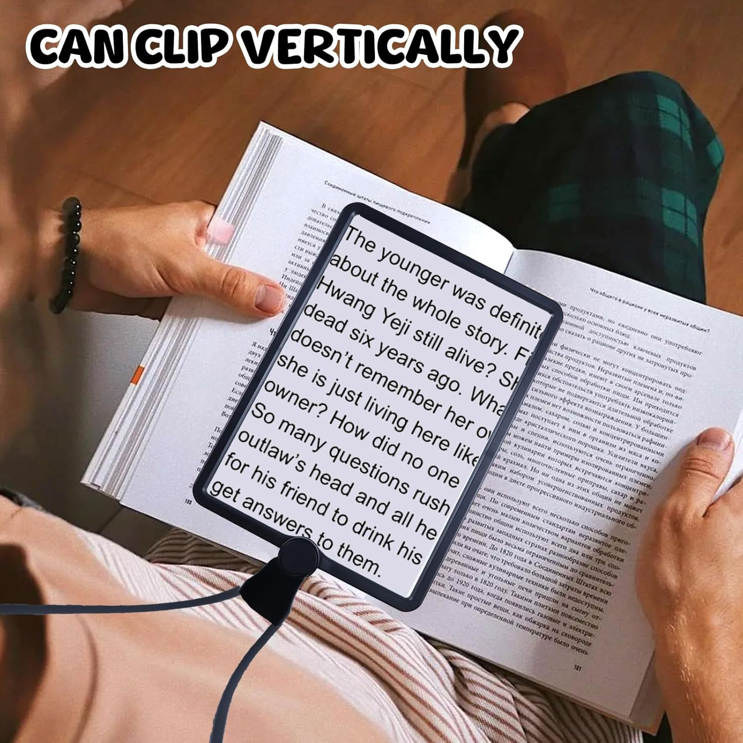 Person hält eine rechteckige Lupe über ein offenes Buch mit Text, im Hintergrund ist ein Holzboden zu sehen.